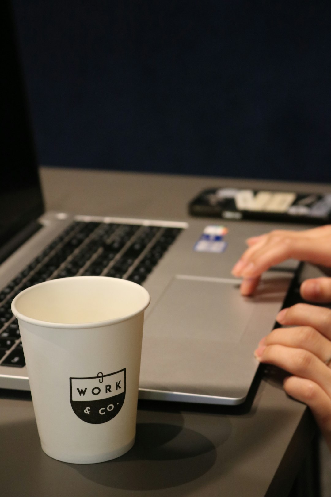 A person typing on a laptop with a cup of coffee in front of them